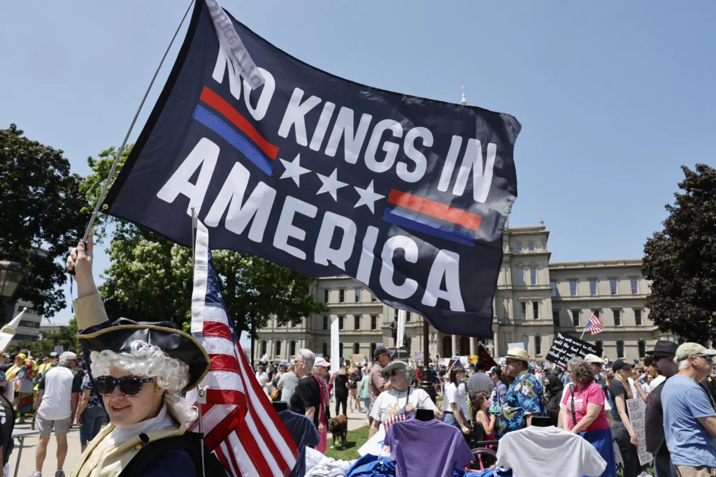 Current image: Crowd of protesters holding a large ‘No Kings in America’ banner amid dense urban demonstration.