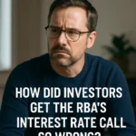 Current image: A thoughtful middle-aged man with glasses and a neatly groomed beard sits indoors wearing a navy blue sweater. He looks slightly concerned, with furrowed brows, as natural light filters through a nearby window. Bold text at the bottom of the image reads, "HOW DID INVESTORS GET THE RBA'S INTEREST RATE CALL SO WRONG?"