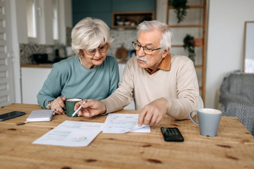 Current image: Senior couple sitting at a kitchen table reviewing Social Security statement and tax forms.