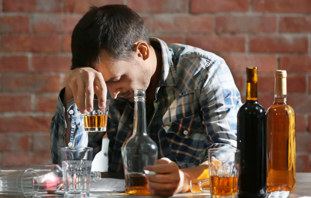 667335209c4a5f5fc2907150_A man in distress holds his head in despair while consuming alcohol
